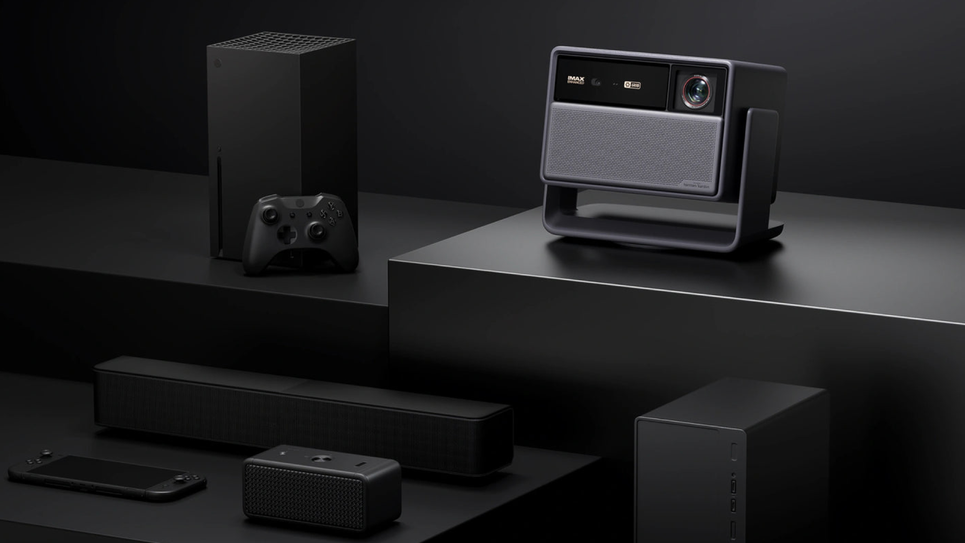  Xbox Series X, soundbar, bluetooth speakers. They're moodily lit on a multi-level black surface against a black background