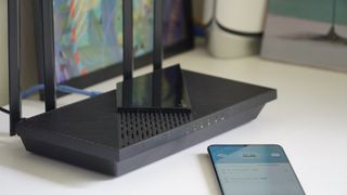 TP-Link Archer AX21 on a table near a phone with the TP-Link app open