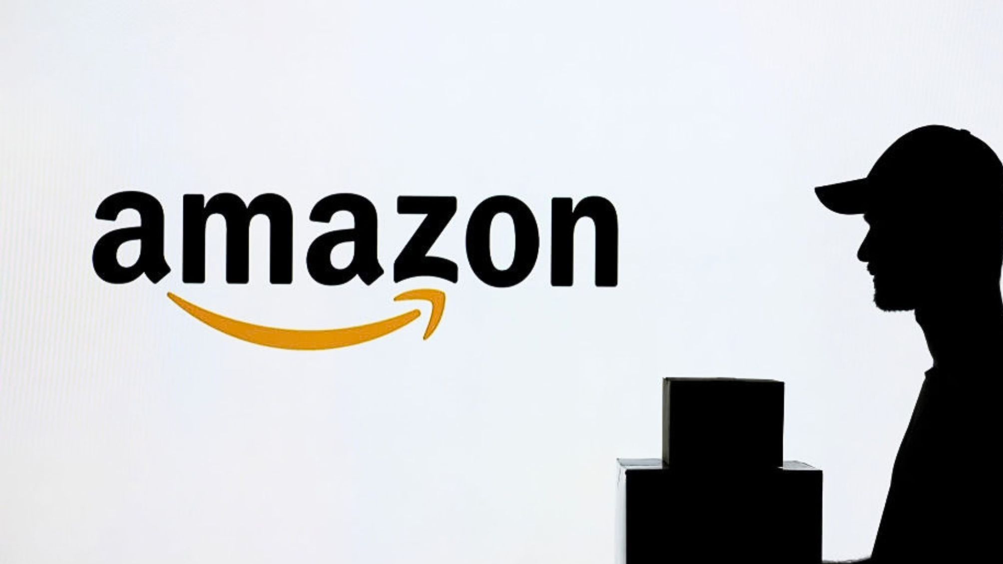 A man carrying a package in front of the Amazon logo 