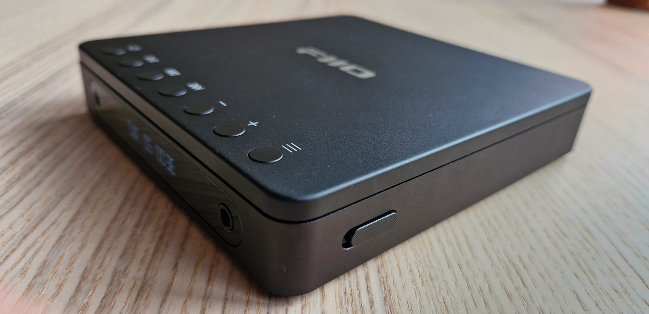 An isometric shot of the FiiO DM13 portable CD player sitting on a wooden table with its lid closed.