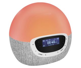 A Lumie Bodyclock Shine 300 on a white background. The clock has a digital screen showing the time and radio station, and a the light is set to a dark pink