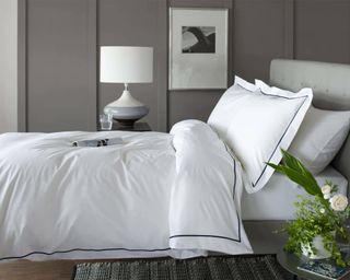 A white cotton duvet cover and pillowcase with a blue embroidered border in a grey panelled bedroom