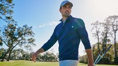 A golfer wearing a blue midlayer on a sunny day