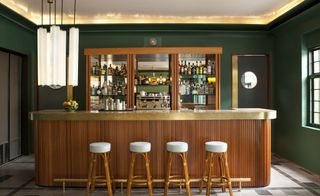 Casa Fayette bar with wood paneled counter, brass top, cane stools and green walls