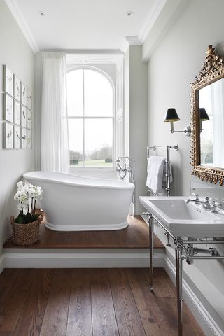 White bathroom with white shutters, bath and sink, wooden floor