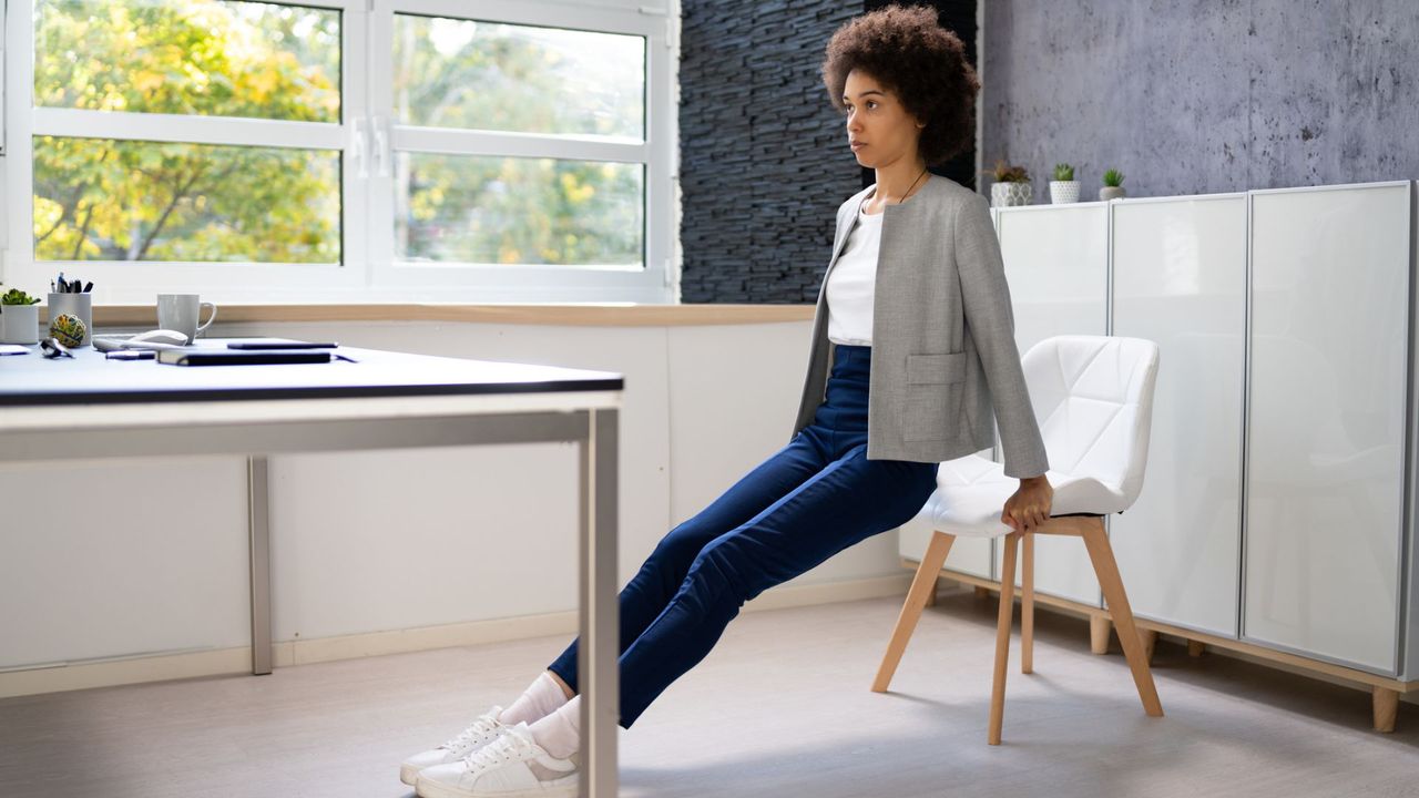 woman in work attire does tricep dips at her desk