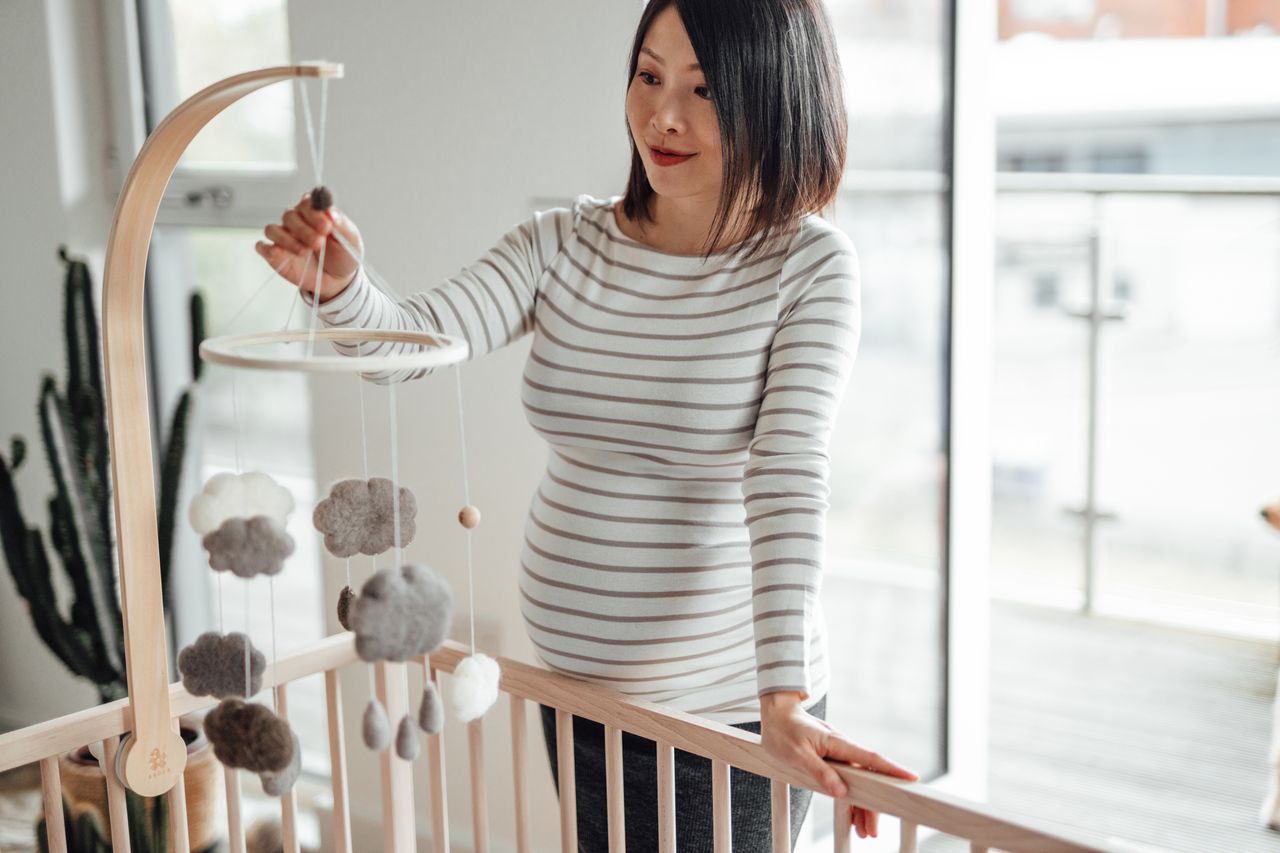 Pregnant Woman Holding A Cot Mobile Toy, Preparing Nursery Bedroom