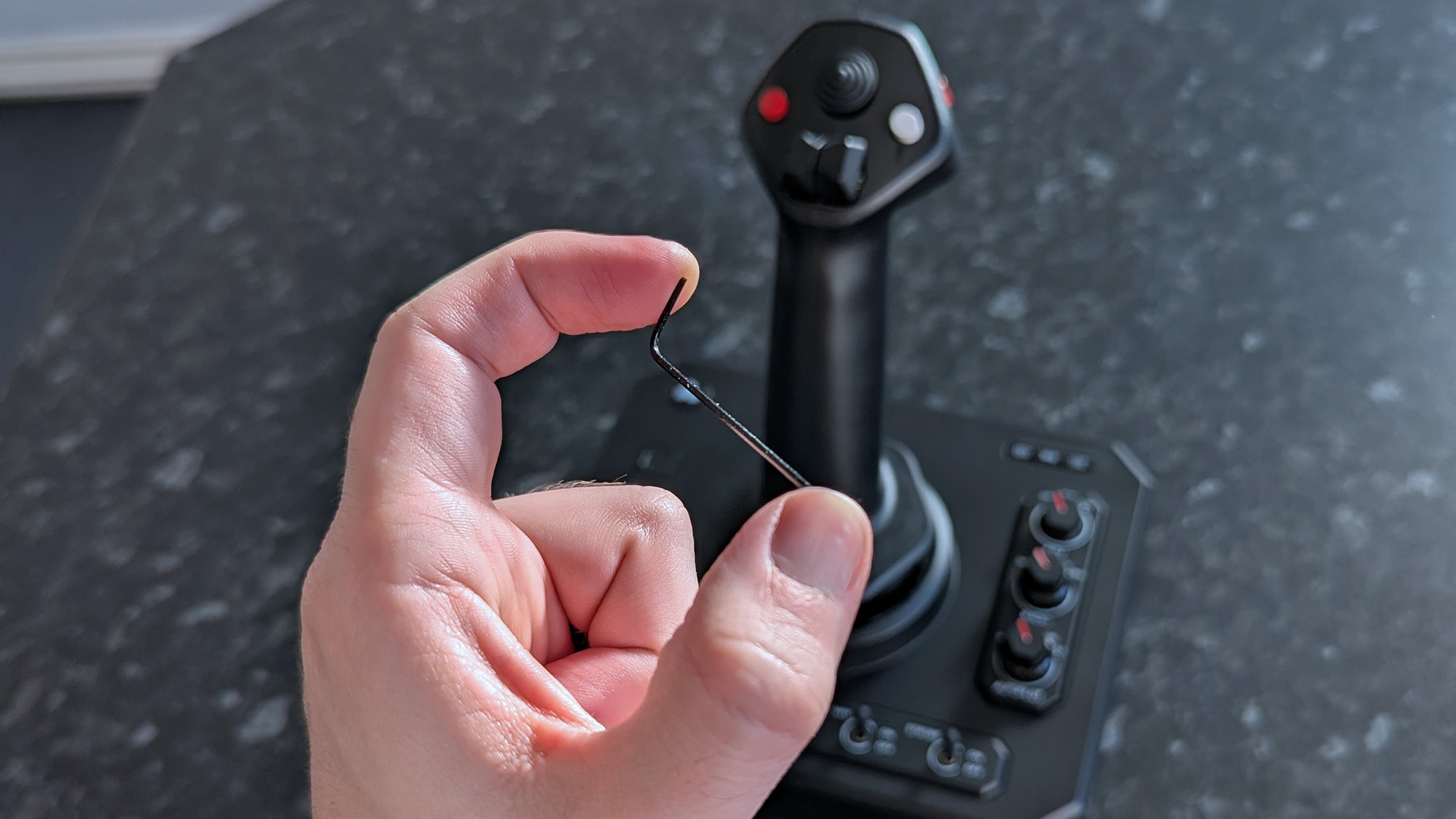 Small hex key held in front of Honeycomb Aeronautical Foxtrot Aviation Stick on a marble-patterned countertop
