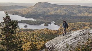 A hiker walks across a rocky summit above a lake on the Appalachian Trail in Maine