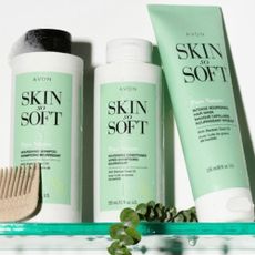 Avon Skin So Soft products sat on a glass shower shelf with a wooden comb and soap bubbles