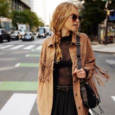 model wears fringe jacket and sheer black skirt standing in the street