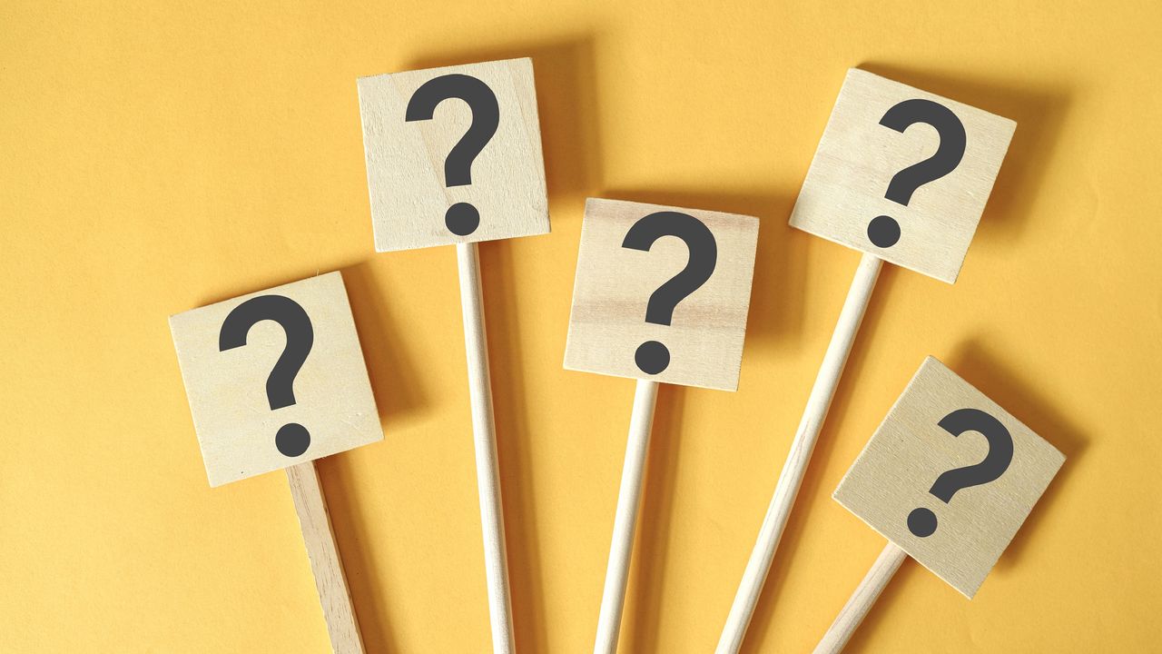 Question marks on wooden blocks mounted on sticks against a yellow background.