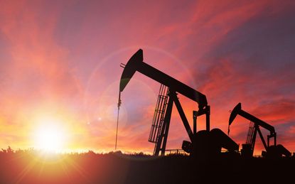 Pump jack silhouette against a sunset sky with deliberate lens flare and copy space. These jacks can extract between 5 to 40 litres of crude oil and water emulsion at each stroke.This image i