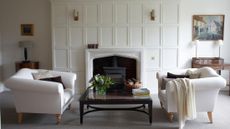 Bright white living room area featuring a pair of white antique-style sofas, a glass-top coffee table, and shaded wall sconces flanking the fireplace