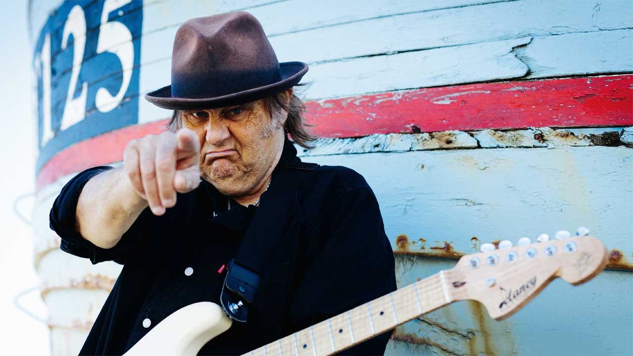 Walter Trout standing in front of a fishing boat, pointing at the camera