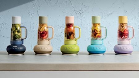 A colourful set of five tumble style drinking cups, upside down on blender bases, against a blue wall