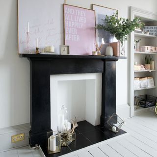 A white-painted living room with white wooden floors and a black fireplace displaying art