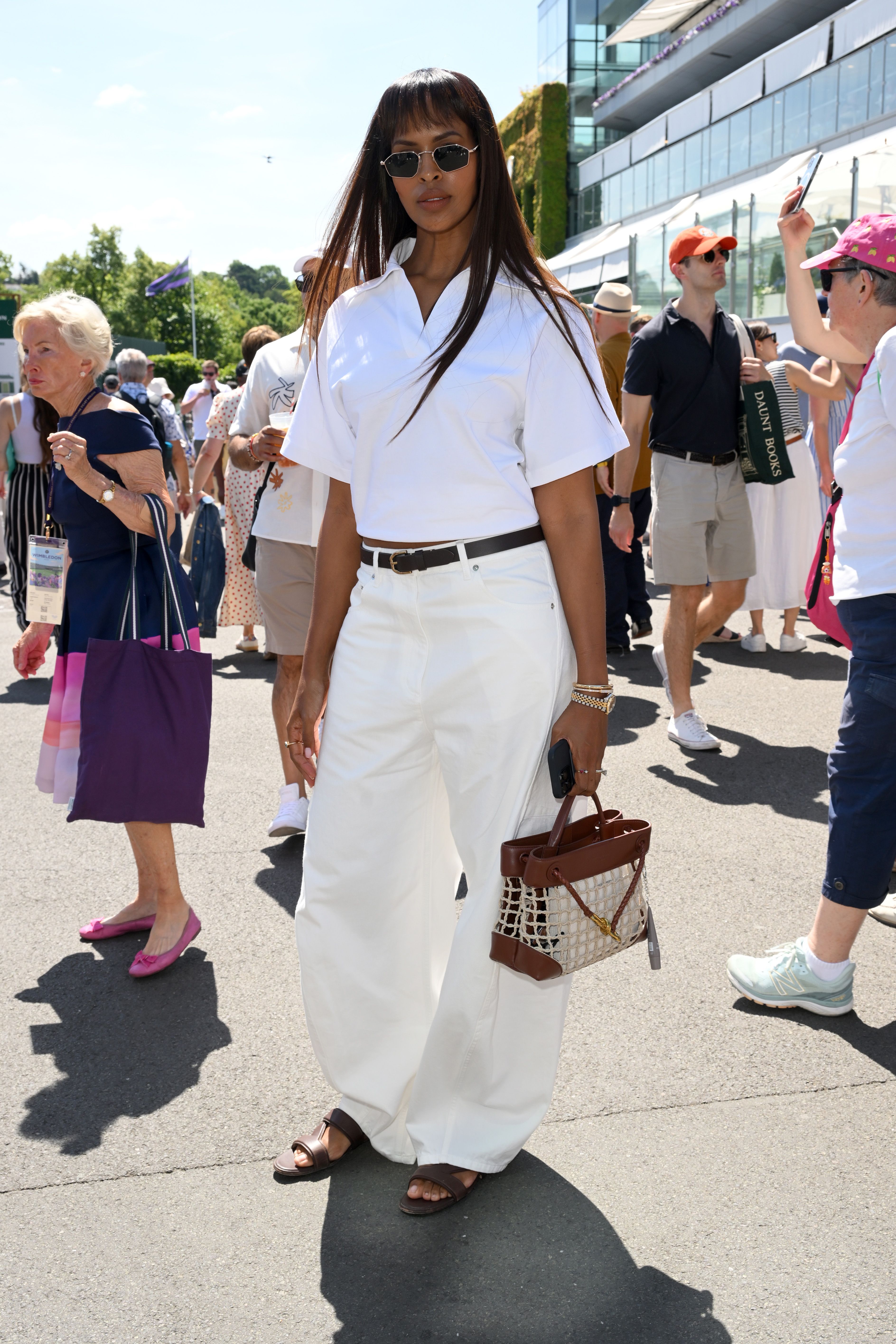 Sabrina Elba wears a pair of white jeans with a white short sleeve shirt, brown belt and brown sandals at Wimbledon in 2025