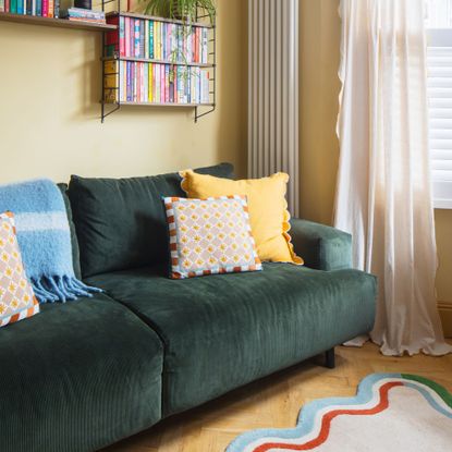 Yellow living room with a green sofa with bright cushions on it