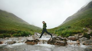 Hiker crossing river in Mountain Valley, Glencoe, Scotland 
