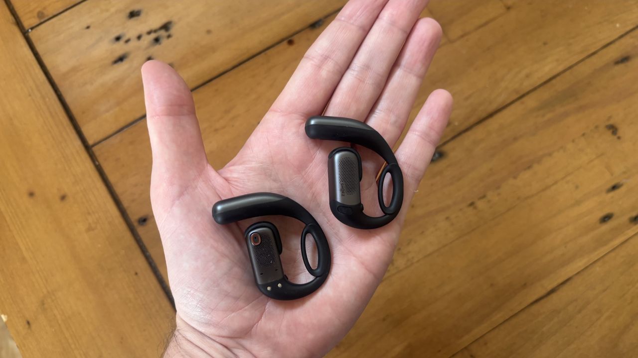 The palm of a hand with the Shokz OpenFit Pro open earbuds resting inside, showing the inner and outer parts of the buds.