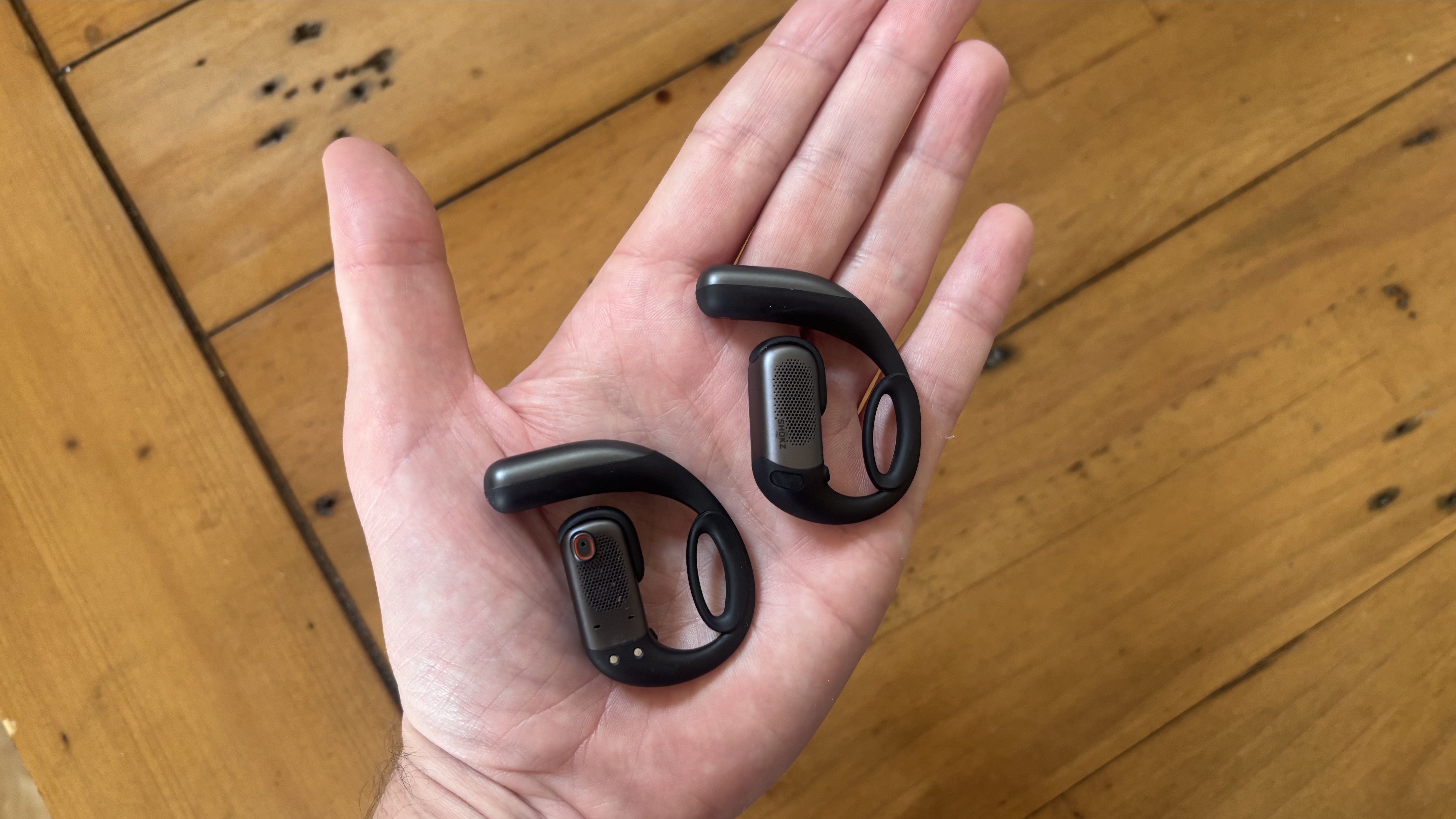 The palm of a hand with the Shokz OpenFit Pro open earbuds resting inside, showing the inner and outer parts of the buds.