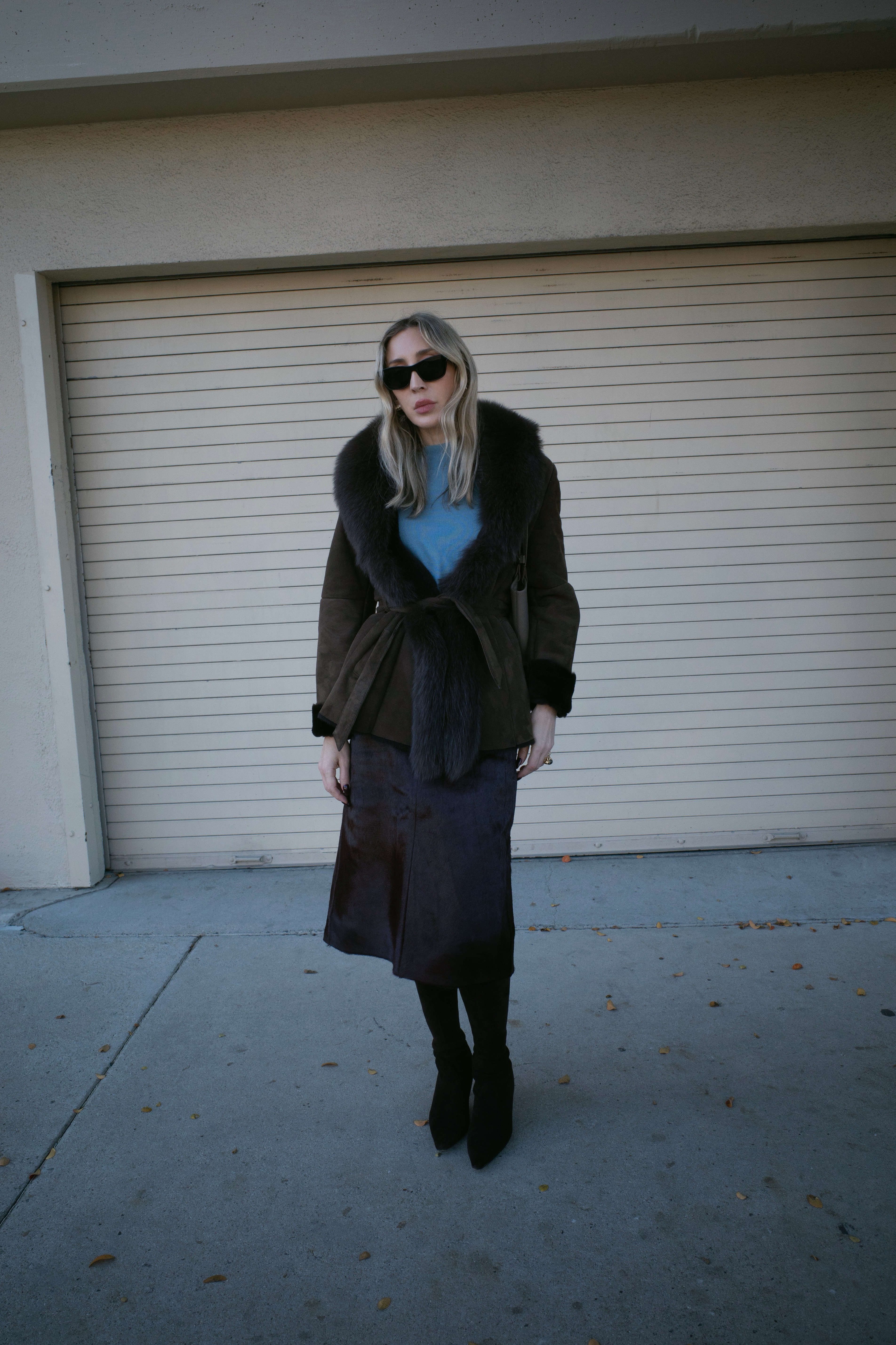 Angela Fink wearing a blue top, a fur coat, and heels