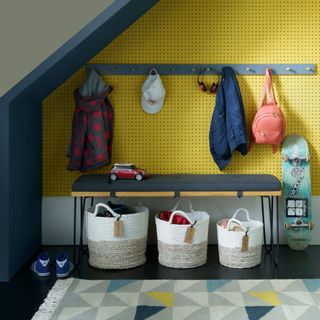 a yellow pegboard decorated hallway area under the staird with coat hooks baskets and a bench and a patterned runner runner