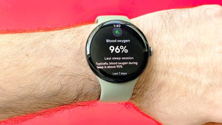 Close-up of the Pixel Watch 5 on a user's wrist against a bright red background