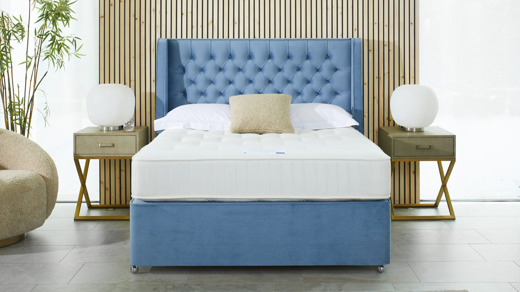 The Travelodge Dreamer Mattress from Sleepeezee on a bed frame in a bedroom, a night stand with a lamp on top sits at either side of the head of the bed