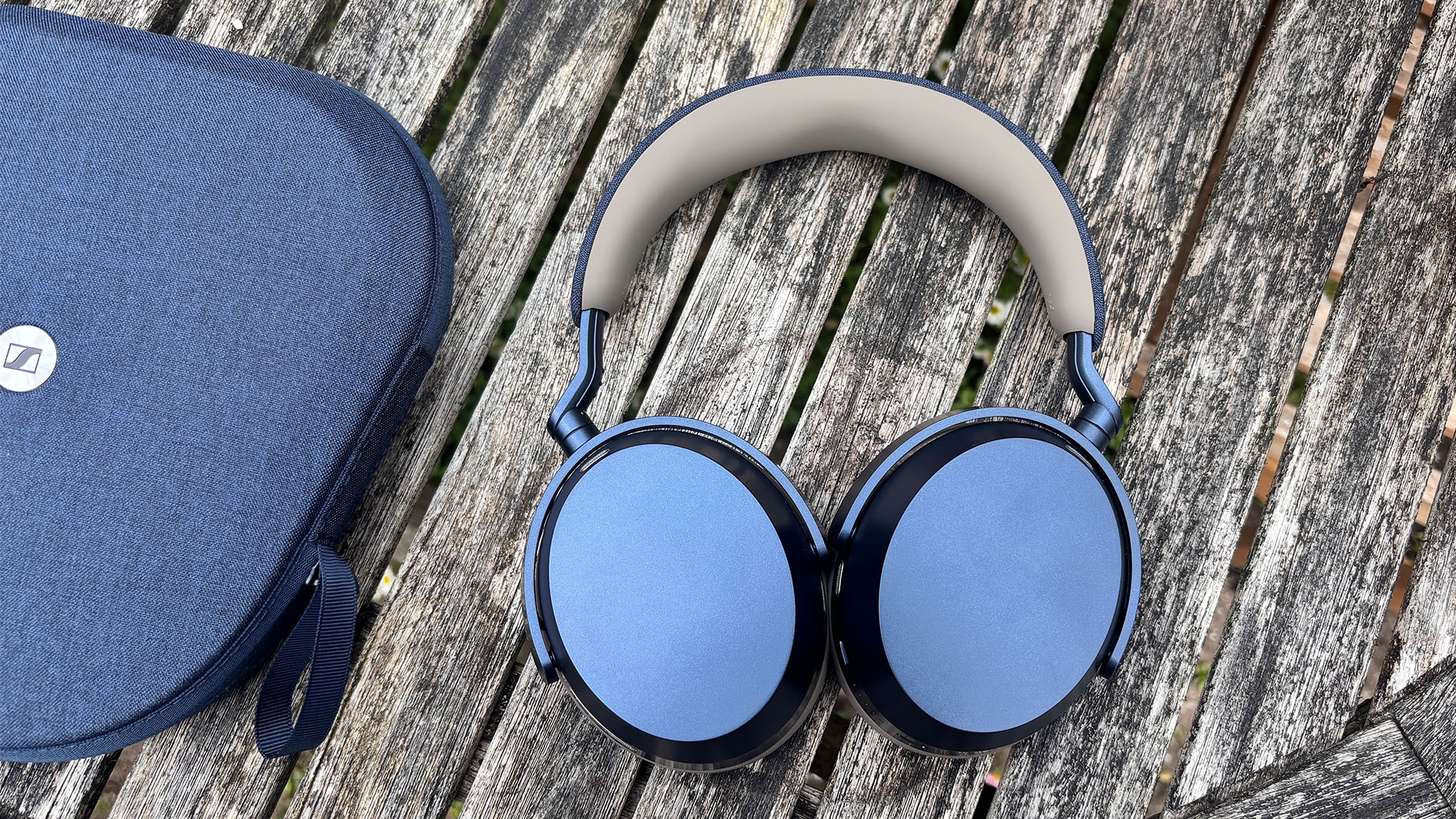 Sennheiser Momentum 5 Wireless wireless headphones earcup-down on wooden garden furniture next to case
