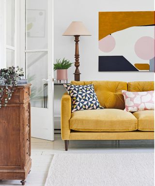 White painted living room with yellow velvet sofa and vintage wooden chest of drawers and cream rug