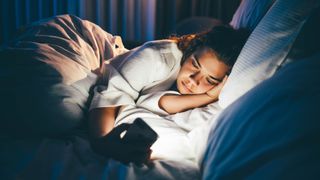A woman wakes up for the fourth time during the night and lies in bed staring at her phone, unable to sleep