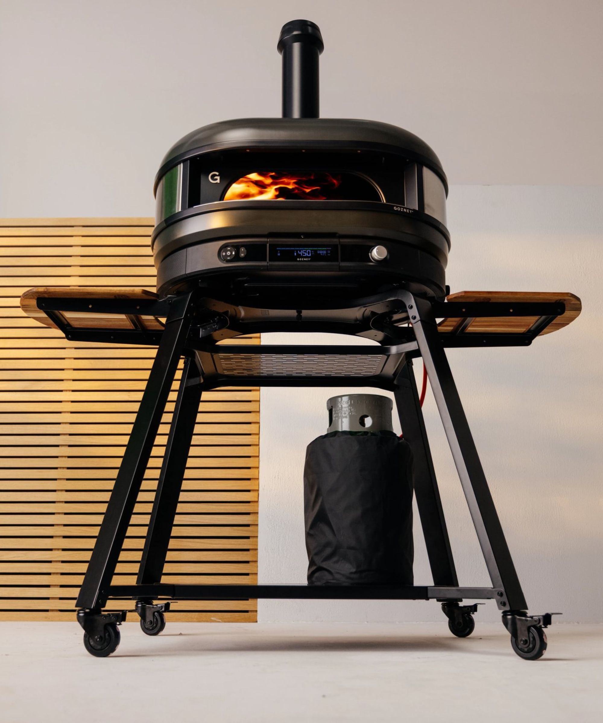 Black pizza oven with gas canister and two wooden serving boards