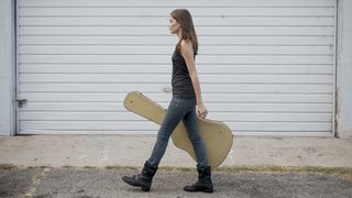Woman walks along the street holding a guitar case