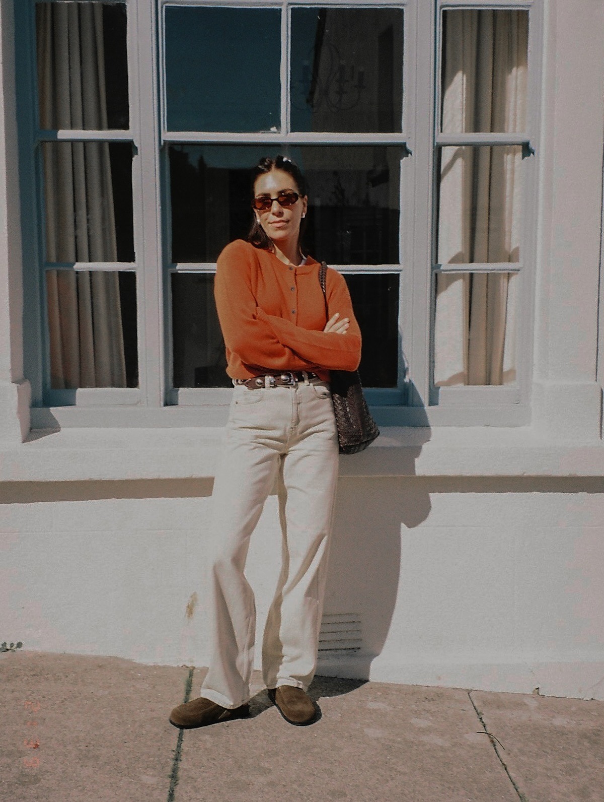 Influencer @_jessicaskye wears a orange cardigan and white jeans with a studded belt.