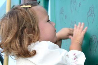 Little girl imitating sign language symbols printed on a board at a playground. 