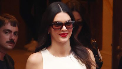 Kendall Jenner between shows at Paris Couture Week wearing tinted sunglasses red lipstick and a white tank top