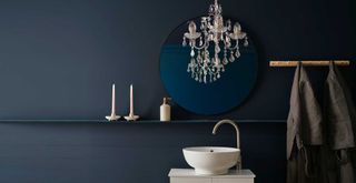 Dark blue bathroom with glass chandelier hung over a sink to show how to make a bathroom look expensive