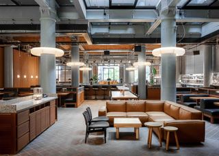 Interior view of Native Manchester featuring a brown L-shaped sofa, tables, chairs, stools and columns with ring lights