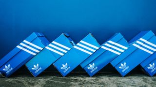 Blue Adidas shoeboxes stacked like dominoes in front of a blue background