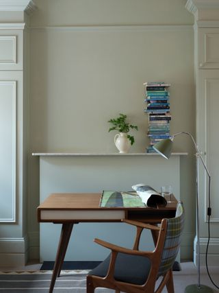 A home office painted in alight green / beige with a mid-century style desk