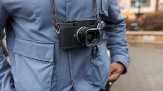 Leica M11 Monochrom digital camera hanging around someones neck on a strap wearing blue shirt