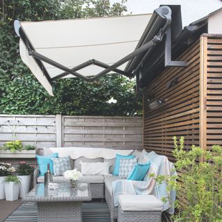 Retractable awning covering outdoor seating area with grey rattan furniture in garden