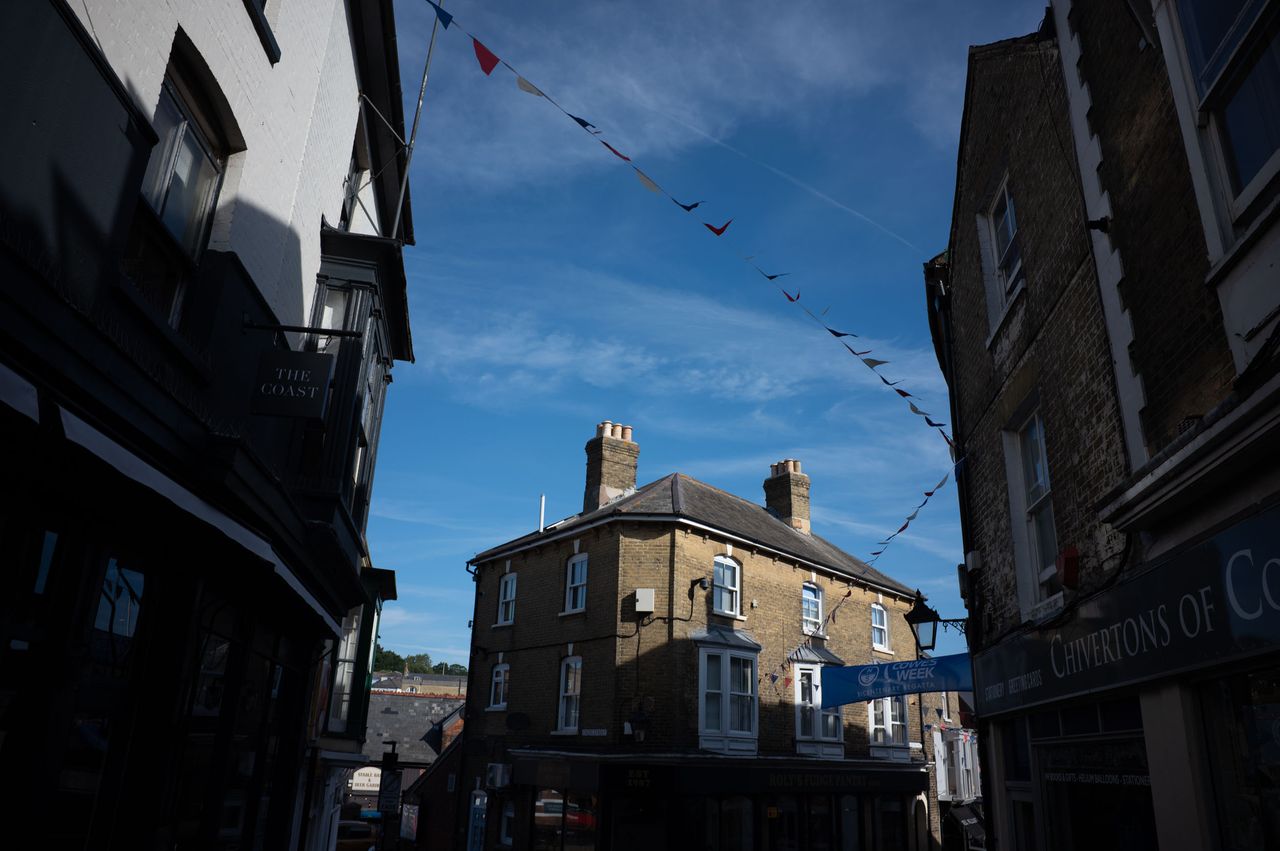 Top of an old building licked by the sun, framed by other buildings in the shade, with bunting leading the eye