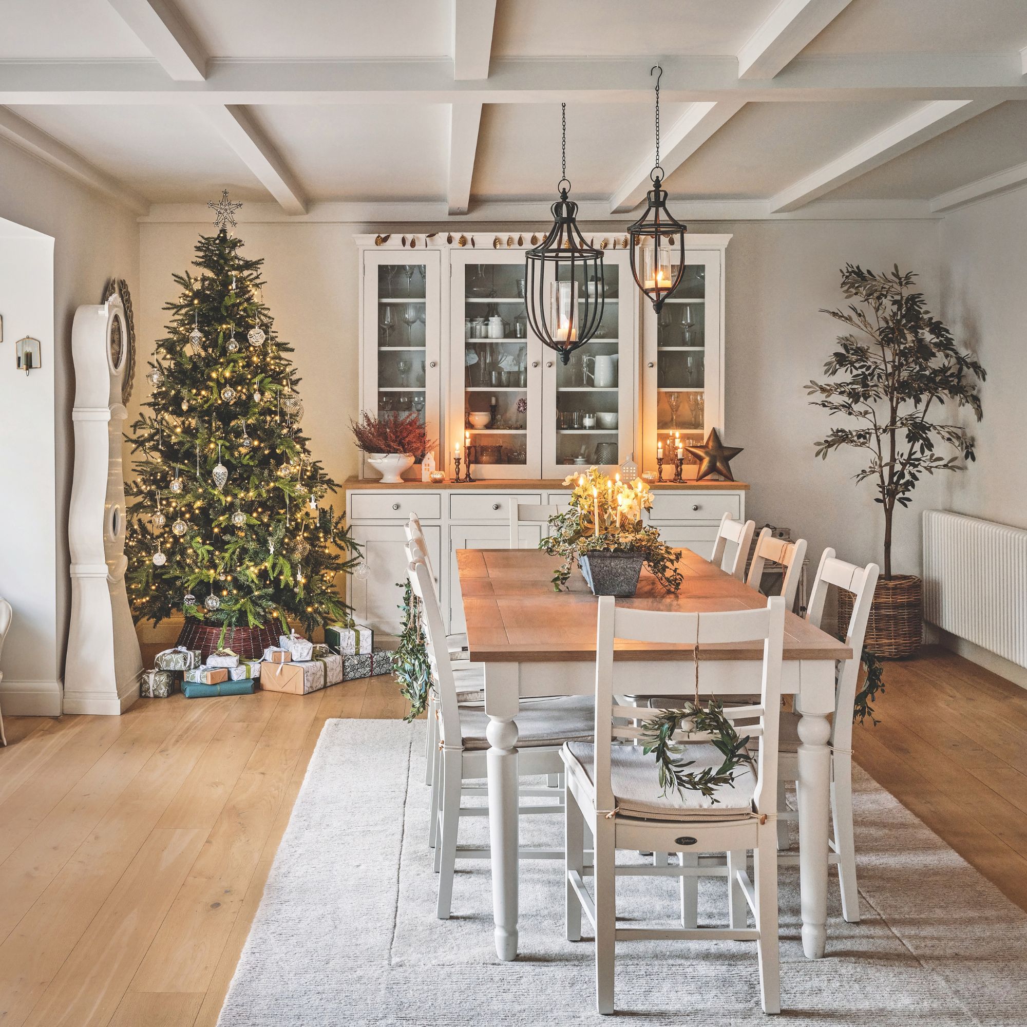 Christmas tree behind a wooden dining room table and next to a wooden storage unit