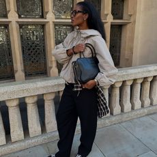 woman wears bomber jacket, plaid shirt and black trousers with a black leather handbag. 