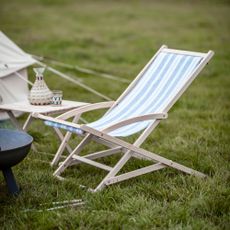 A blue and white striped deckchair sat on the grass next to a tent and small table