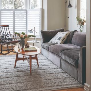 grey living room with wall-mounted picture frames with a cream-colored sofa with soft neutral, delicately patterned cushions on a grey carpet next to a white table topped with candles and tea