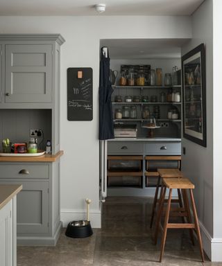 An example of kitchen storage ideas showing a kitchen with gray cabinets and two wooden bar stools against the wall